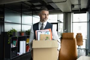 businessman in suit carrying cardboard box with belongings leaving office